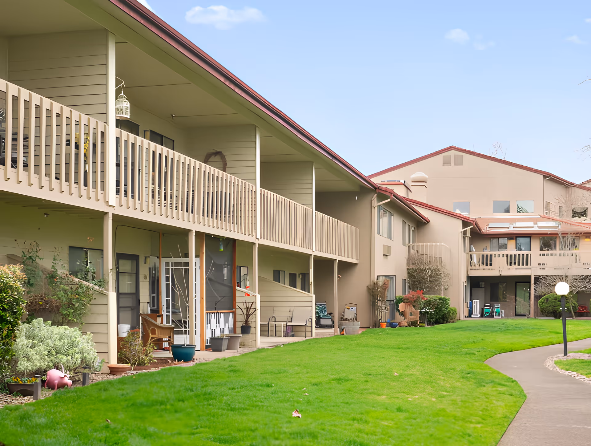 Two-story senior living building with covered balconies overlooking a green lawn and paved walkway.