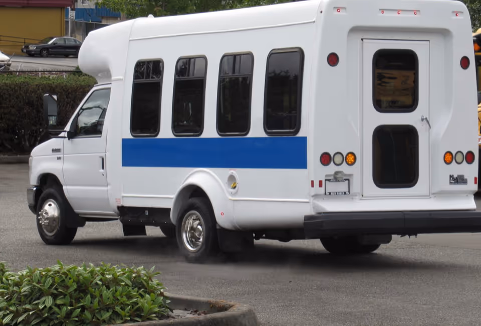 White passenger shuttle bus with a blue stripe parked in a lot.