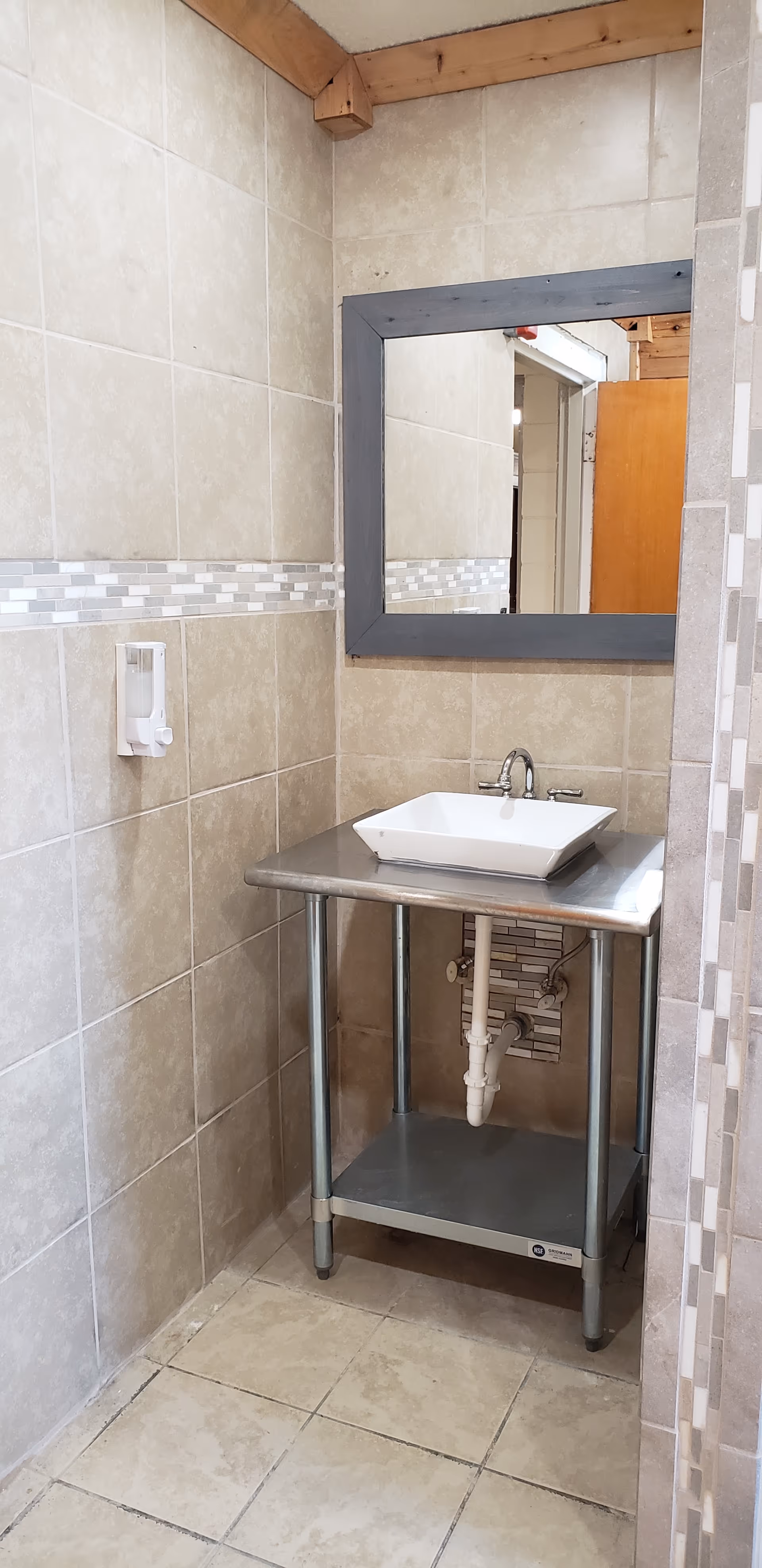 Small tiled bathroom with a metal sink vanity, mirror, and exposed plumbing.