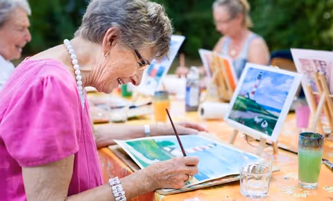 Older adults painting at an outdoor art session with easels and supplies.