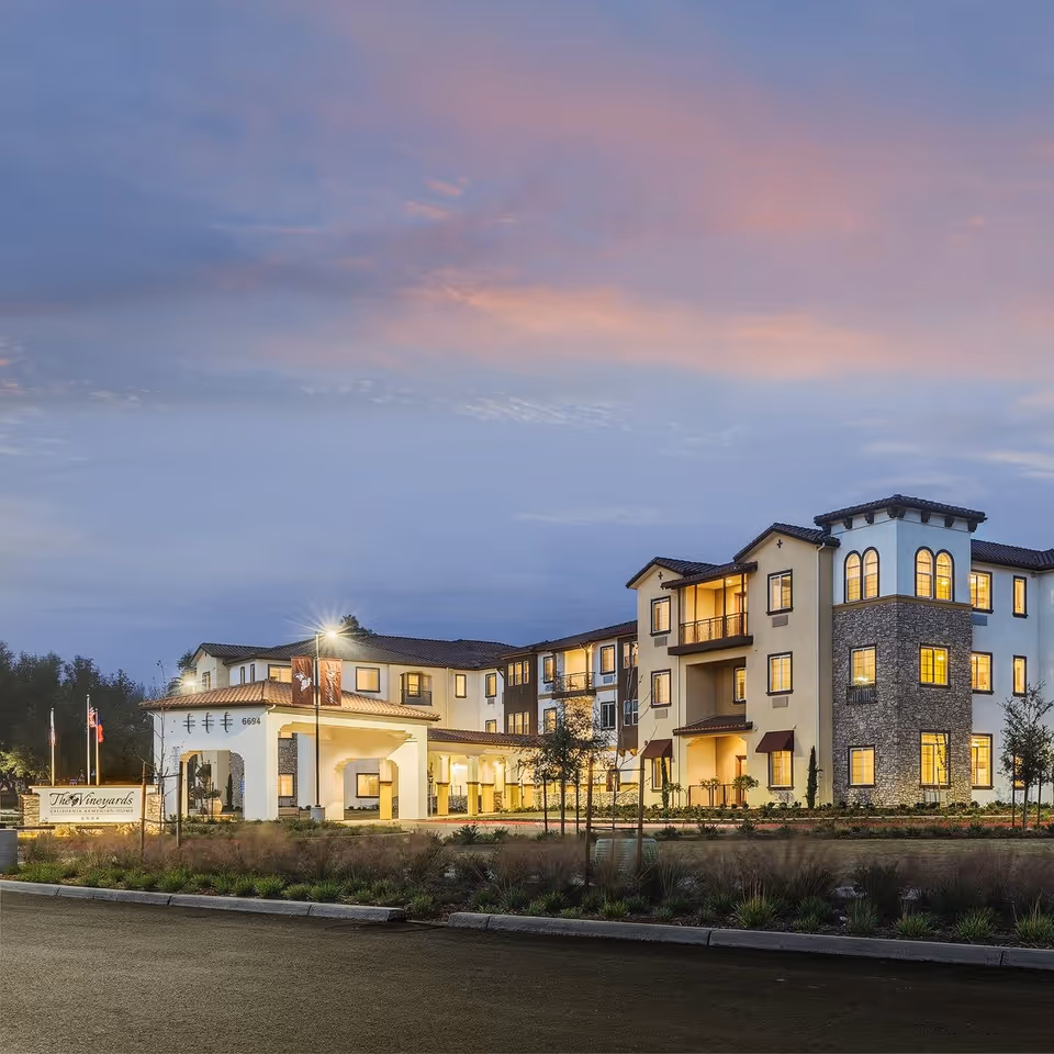 Exterior view of The Vineyards Cognitive Care Community at dusk with lit windows.