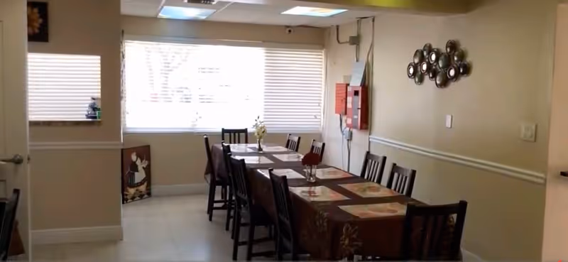 A dining room with a long table, chairs, and window blinds in a retirement home.