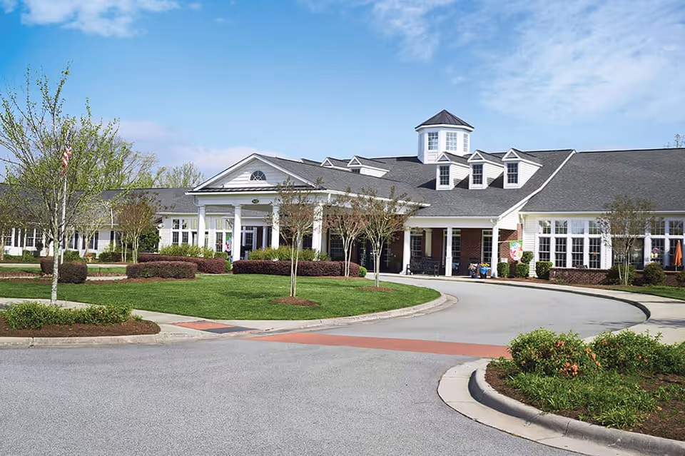 Sunny exterior view of Spring Arbor of Greensboro, showing entrance, circular driveway, and landscaped grounds.
