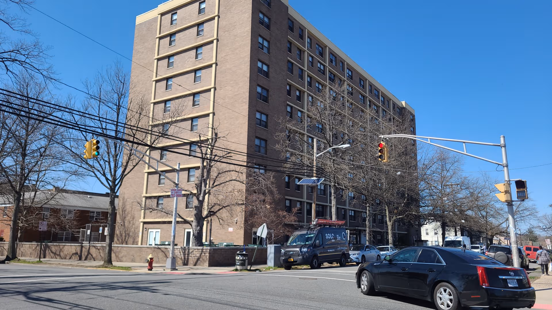 Tall brick senior living building on a city street with cars and leafless trees