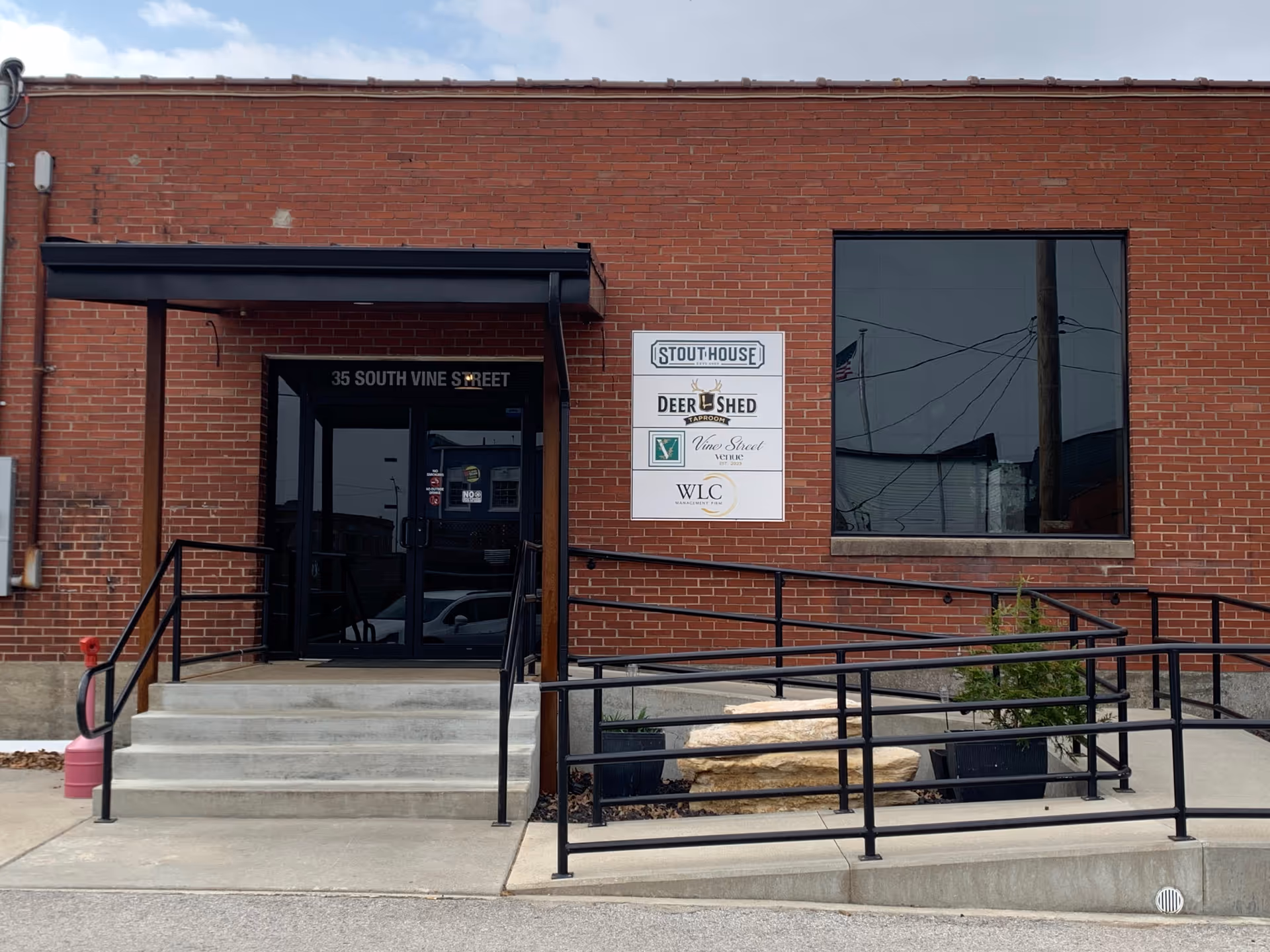 Exterior brick building with glass entry doors, a black awning, ramp, and signs.