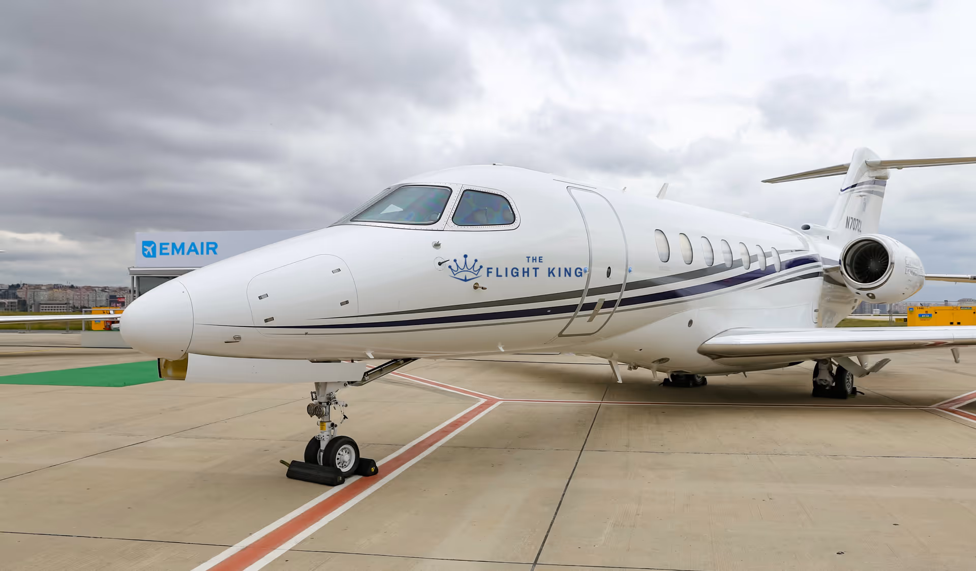 White private jet on a concrete airport apron under a cloudy sky.