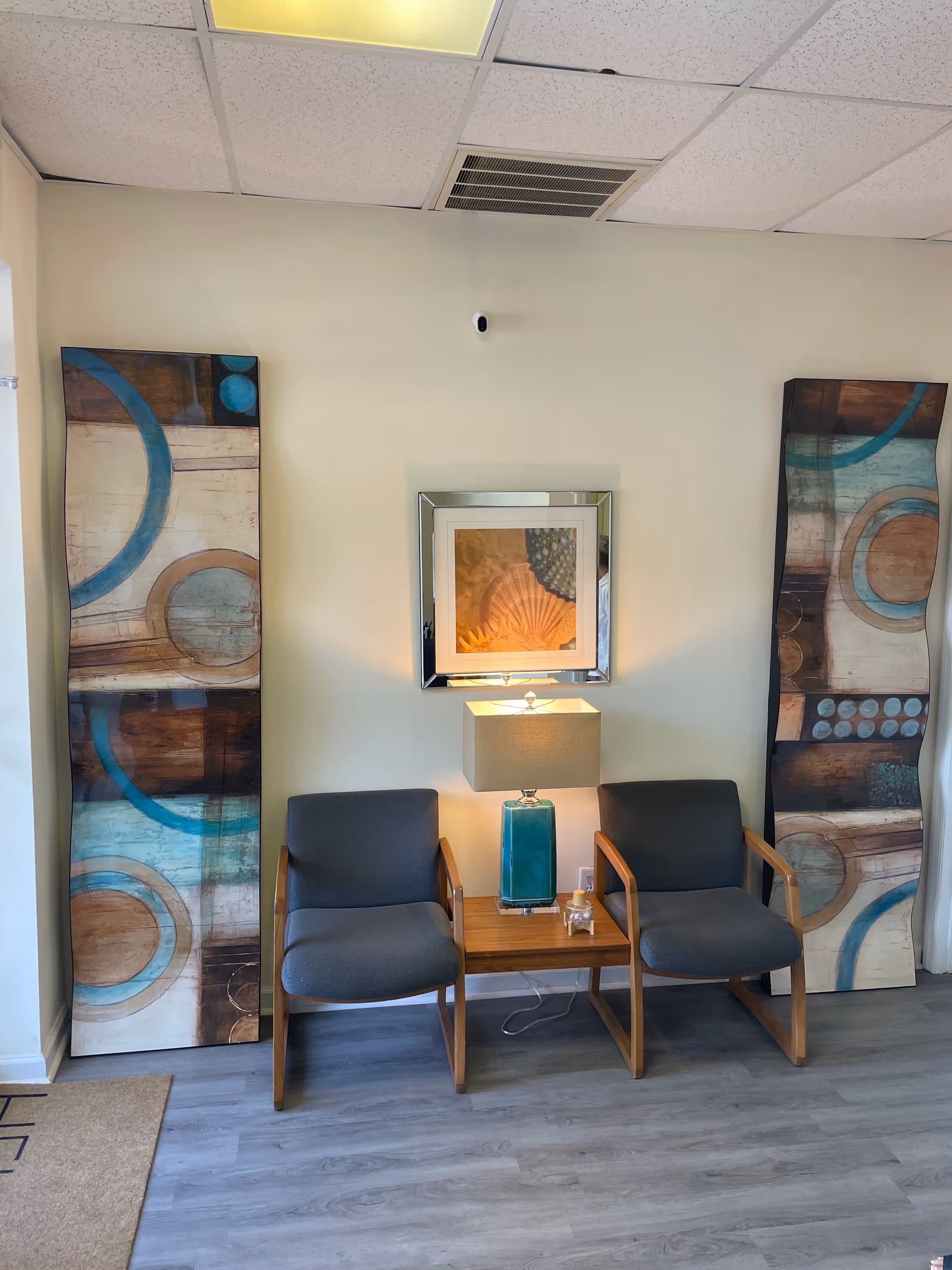 Two blue-armchairs with a wooden table and abstract art in a neutral lobby area.
