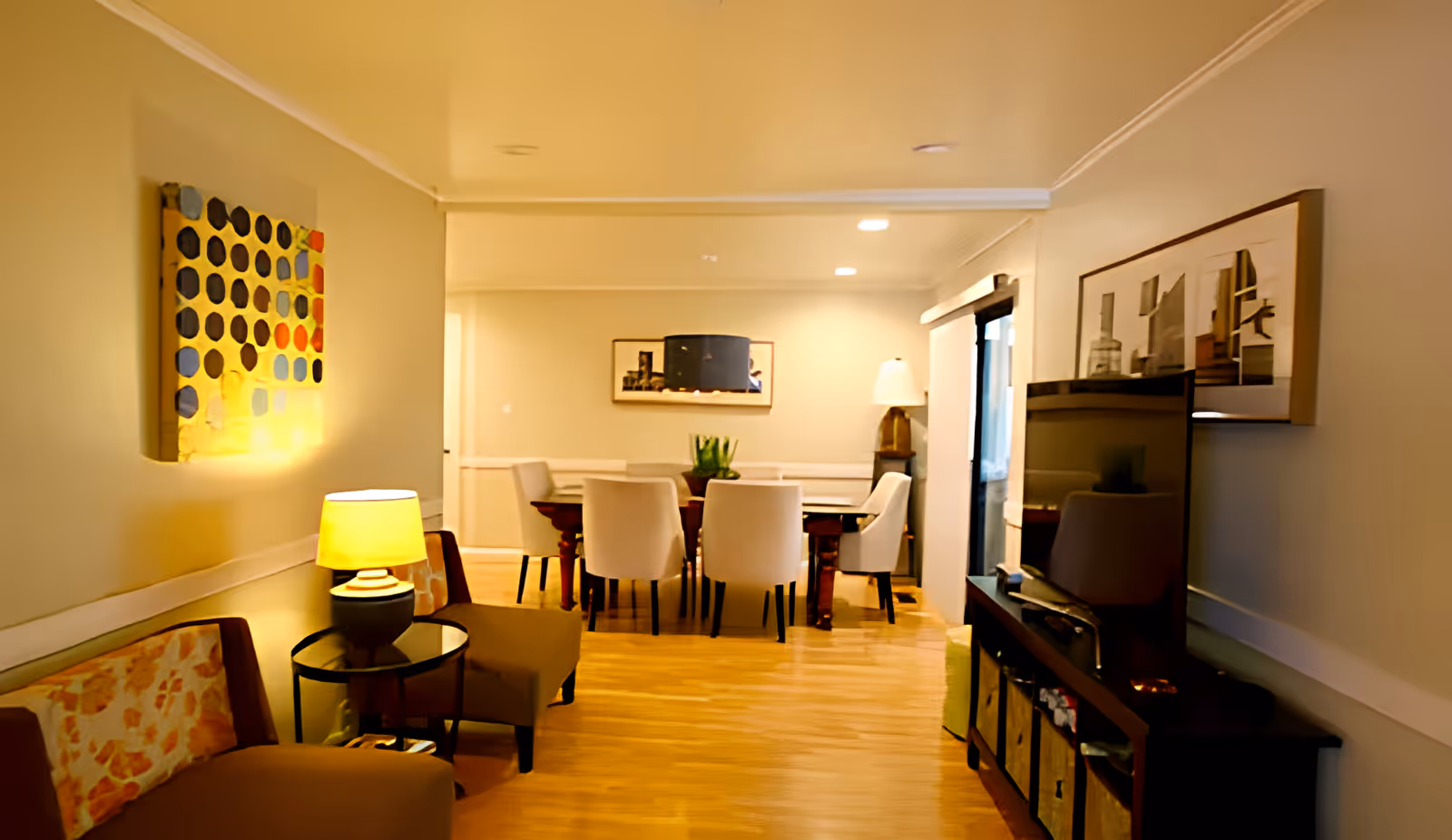 Well-lit combined living and dining area with chairs, a TV console, and a dining table under warm lighting.
