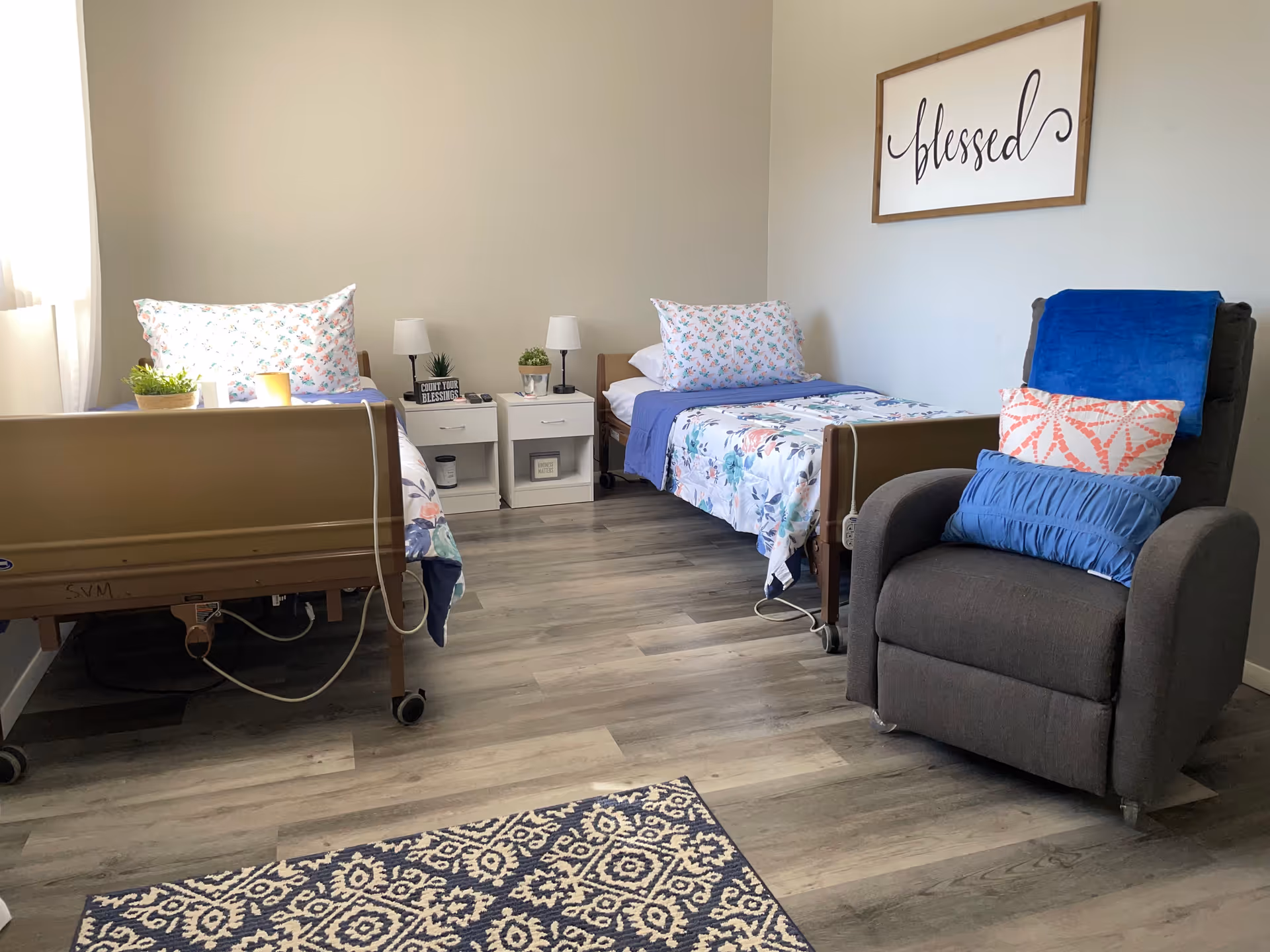 Two hospital beds in a shared senior living bedroom with nightstands and a recliner.