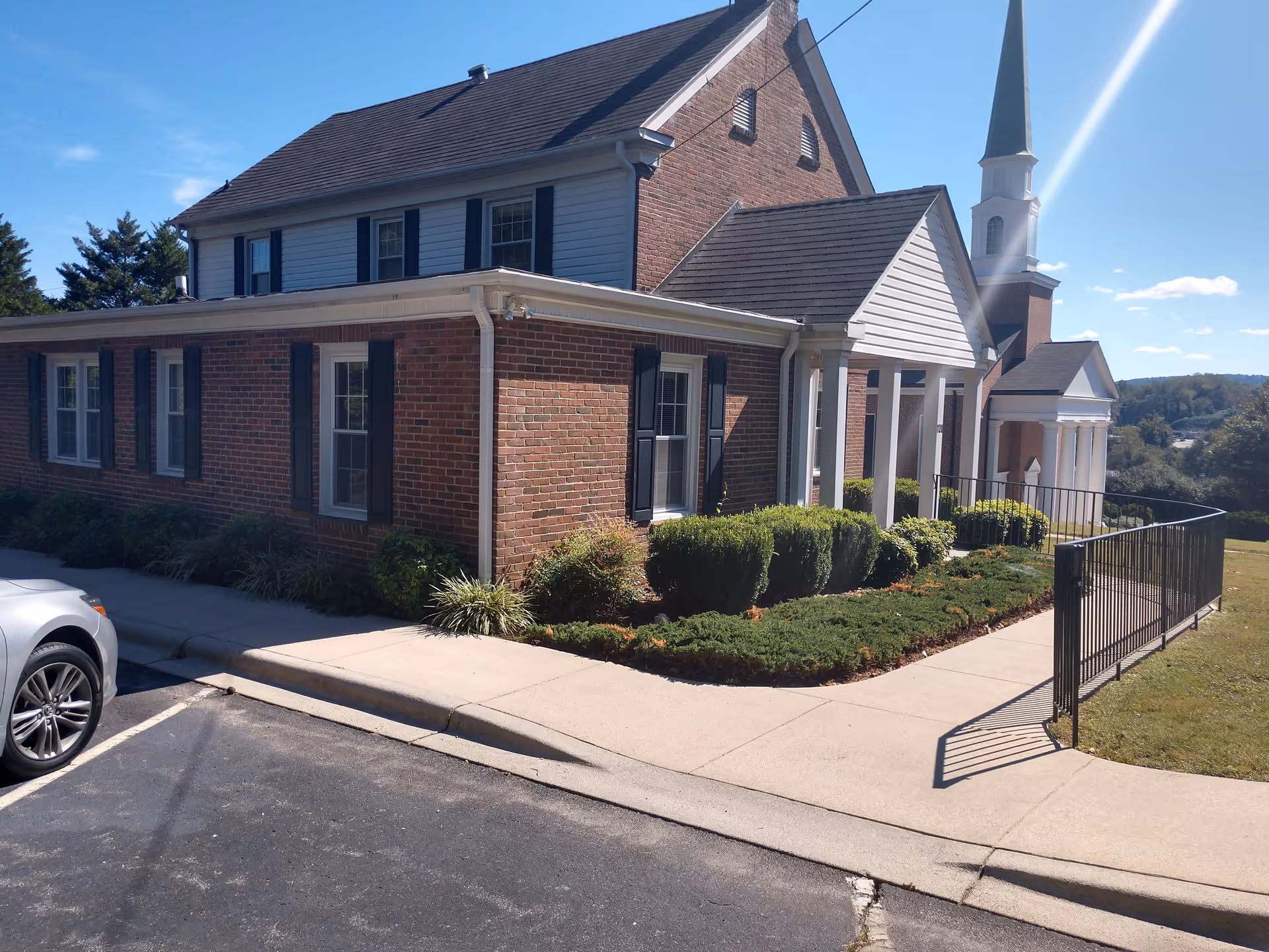 Brick senior living facility exterior with white columns, shrubs, and gated walkway along sidewalk.