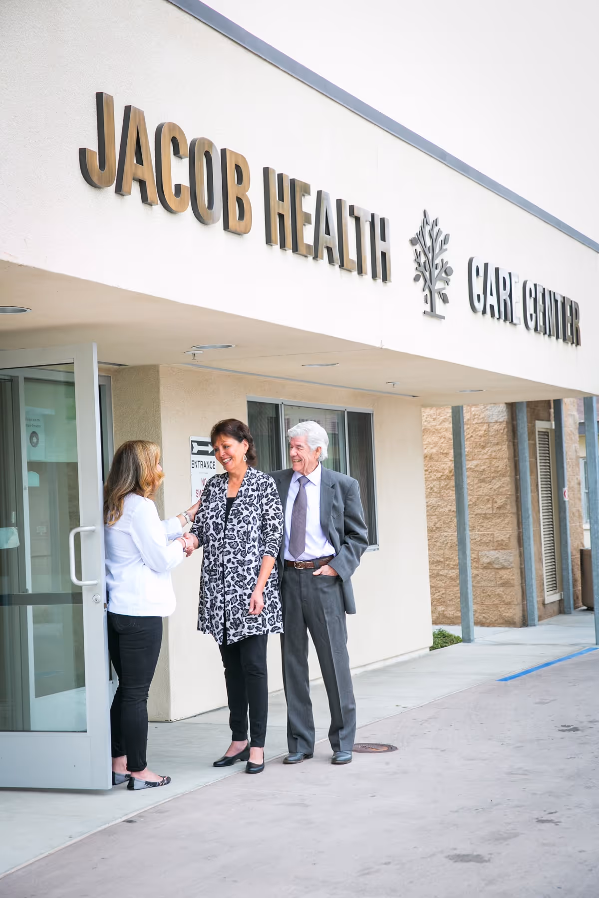 Three people talking at the entrance beneath a 'Jacob Health Care Center' sign.