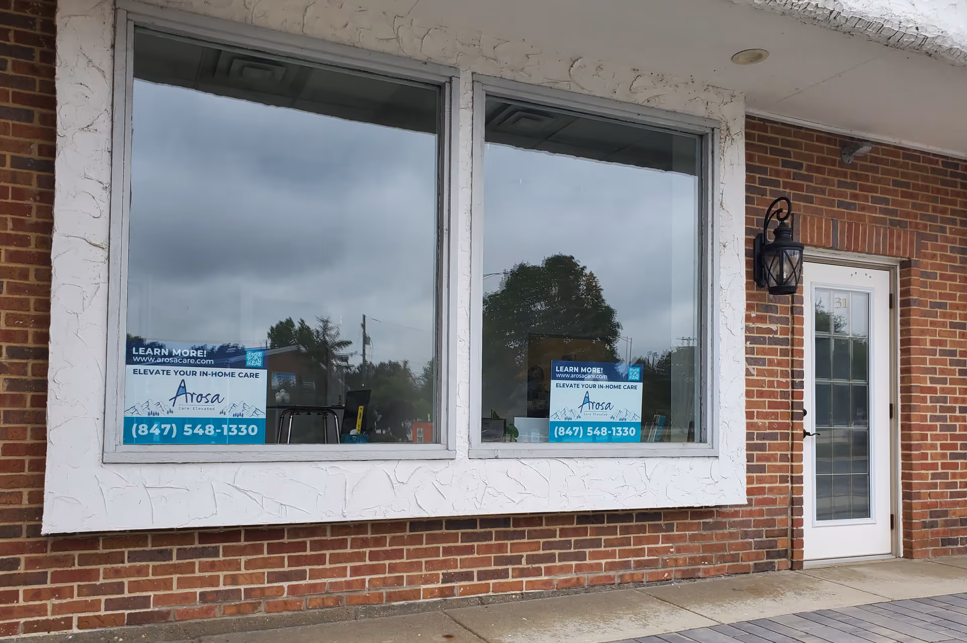 Exterior brick storefront with large windows, a glass door, and signs on the panes.