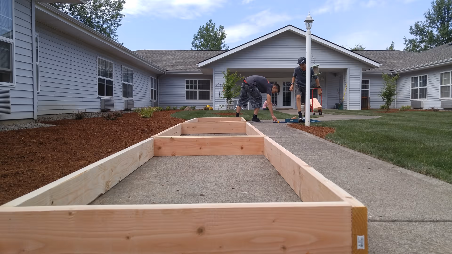 Outdoor construction along a front walkway at Creekside Place Memory Care, workers building wooden frames.