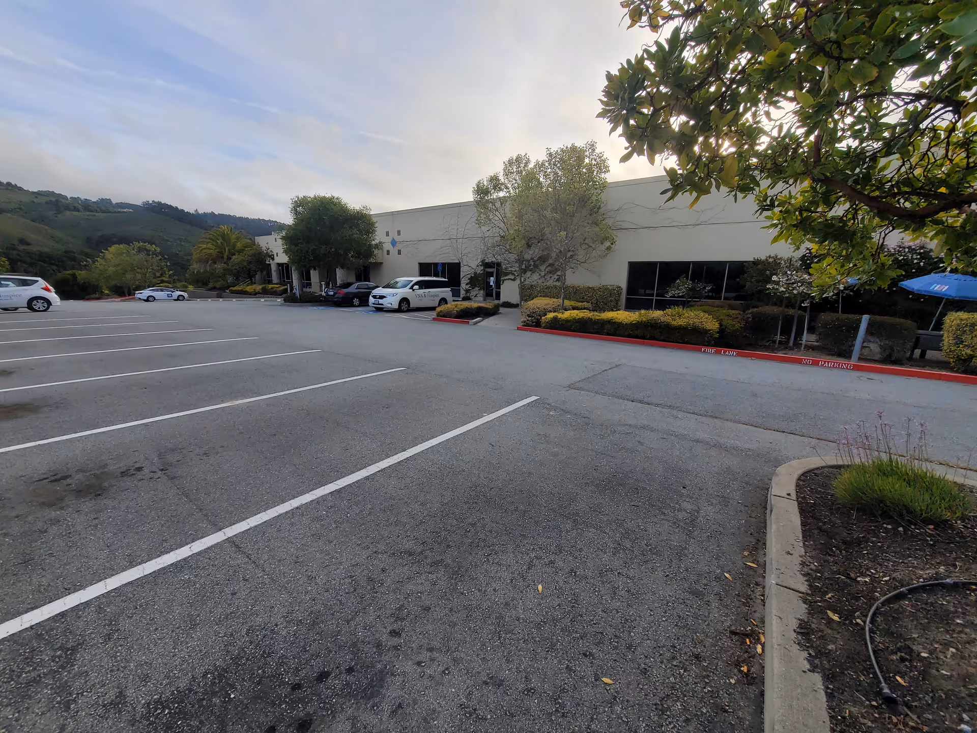 Parking lot in front of Central Coast VNA & Hospice building with trees and shrubs.