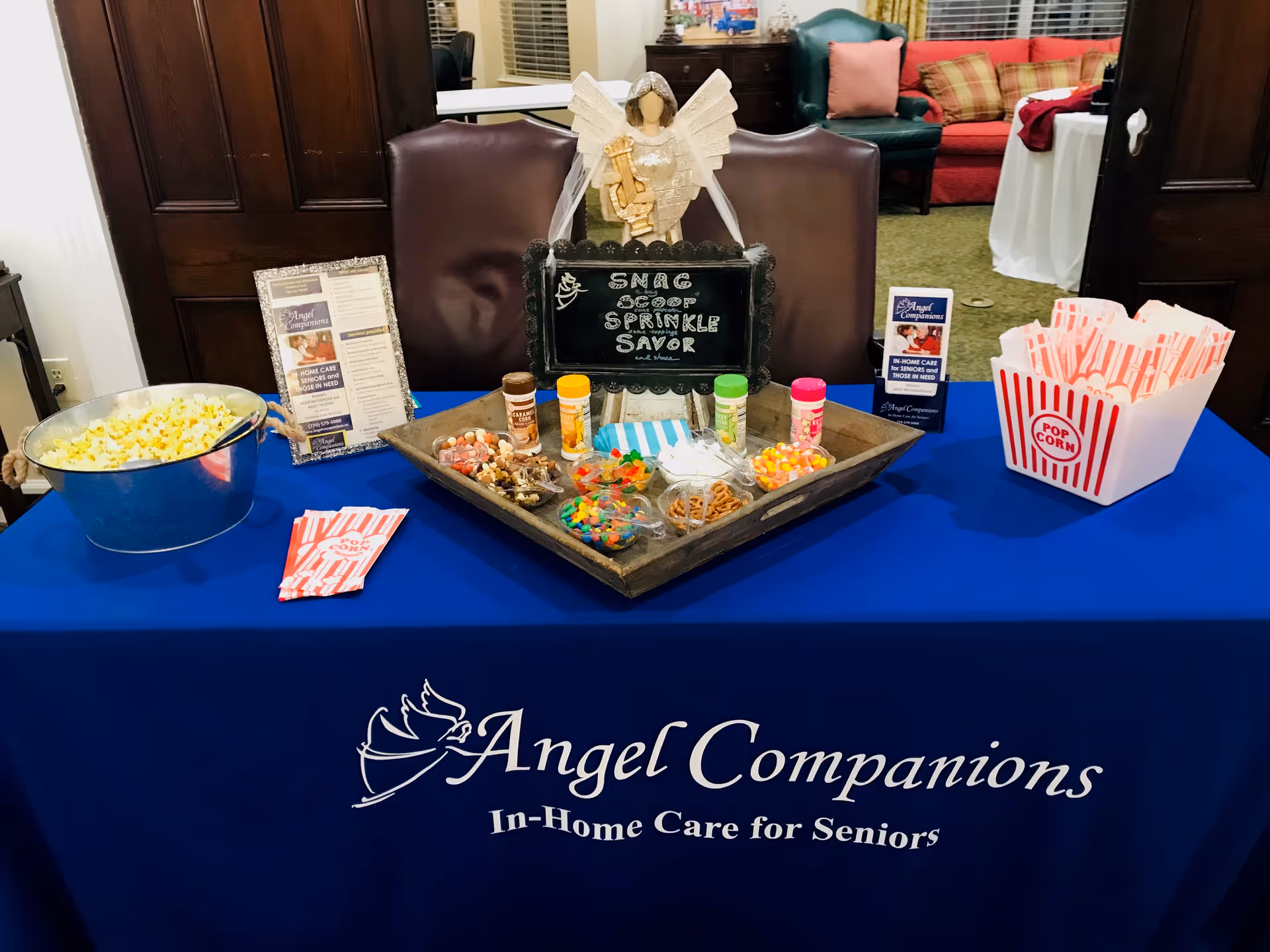 Promotional table with snacks and Angel Companions signage in a senior care facility lobby.