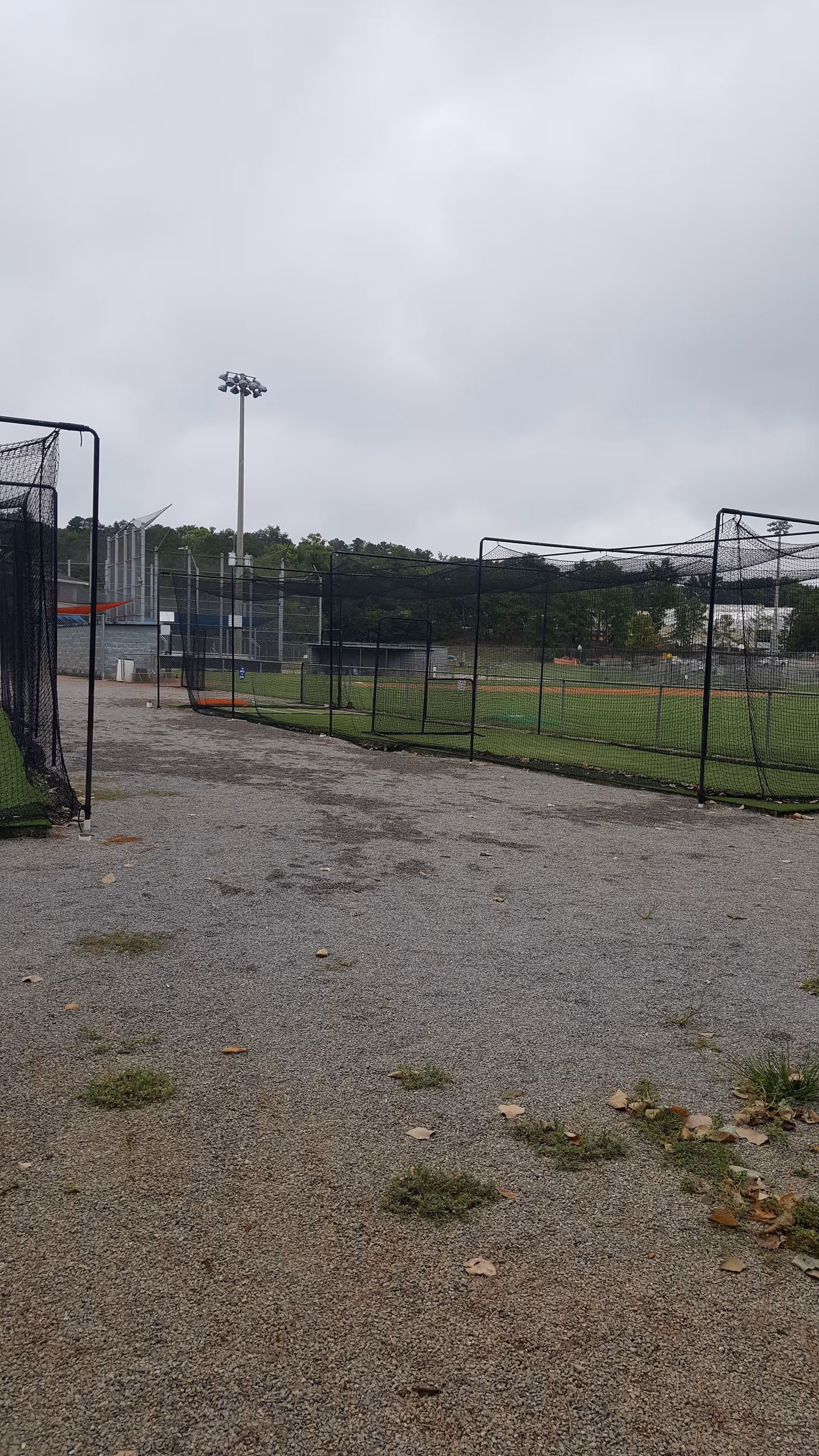 Outdoor gravel path beside fenced sports fields under cloudy sky