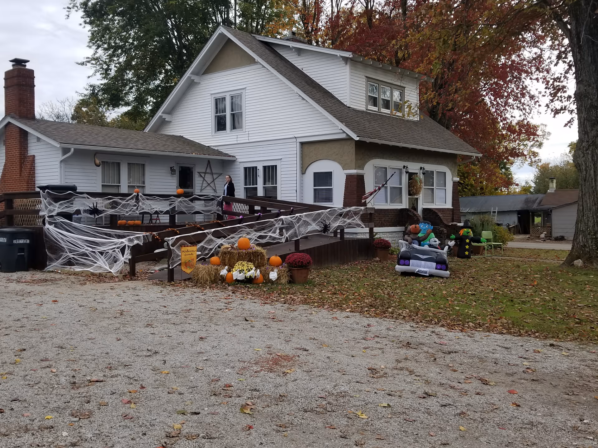 A white two-story house decorated with Halloween spider webs, pumpkins, and yard inflatables.