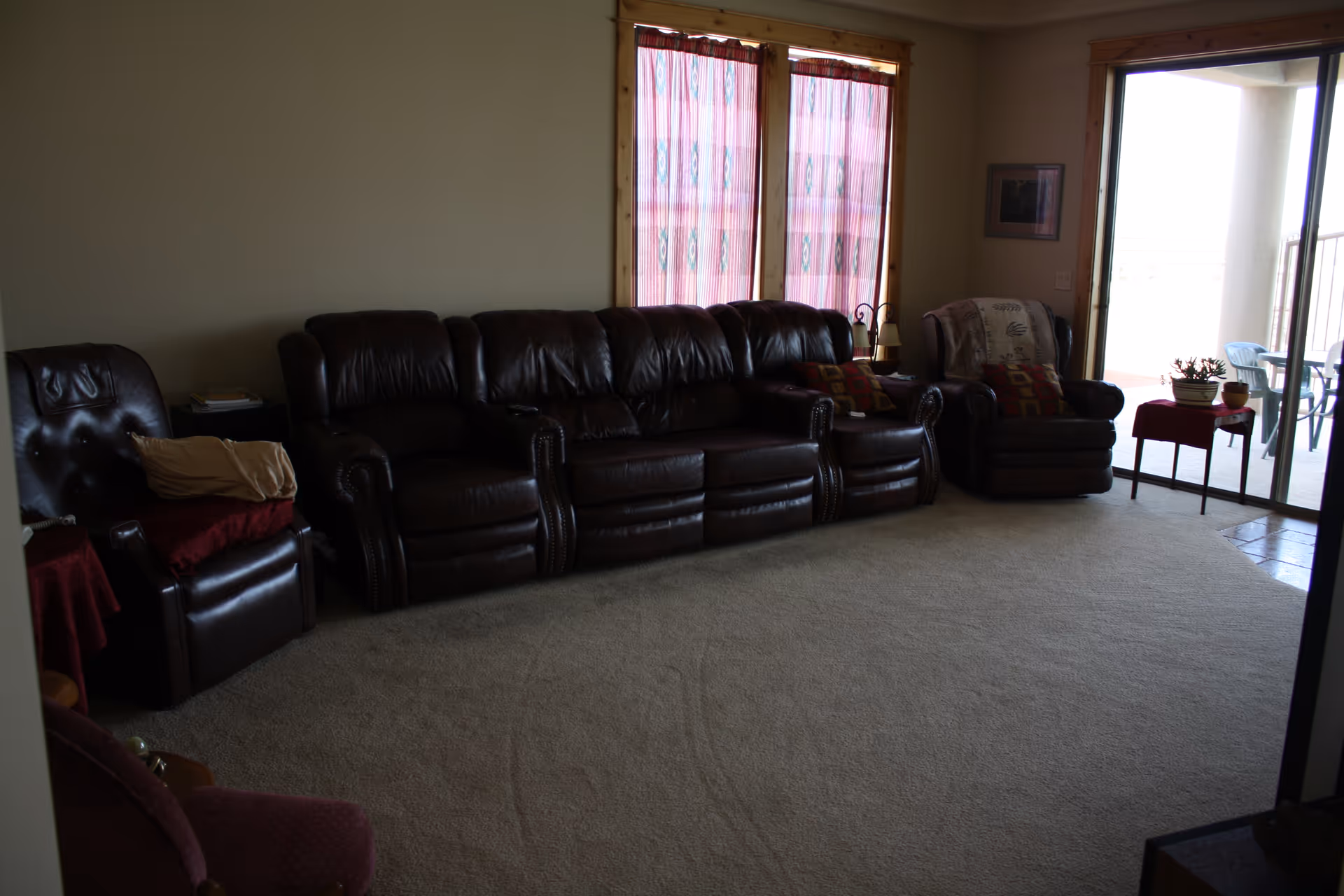 A spacious living room with brown leather sofa set, chairs, and sliding glass door.
