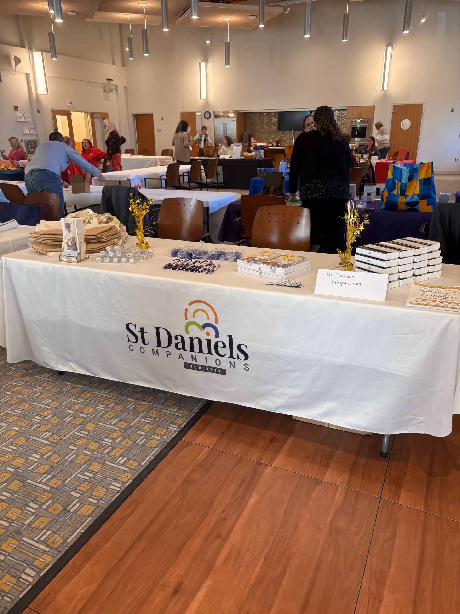 Indoor senior living expo at St Daniels Companions with tables, attendees, and booths.
