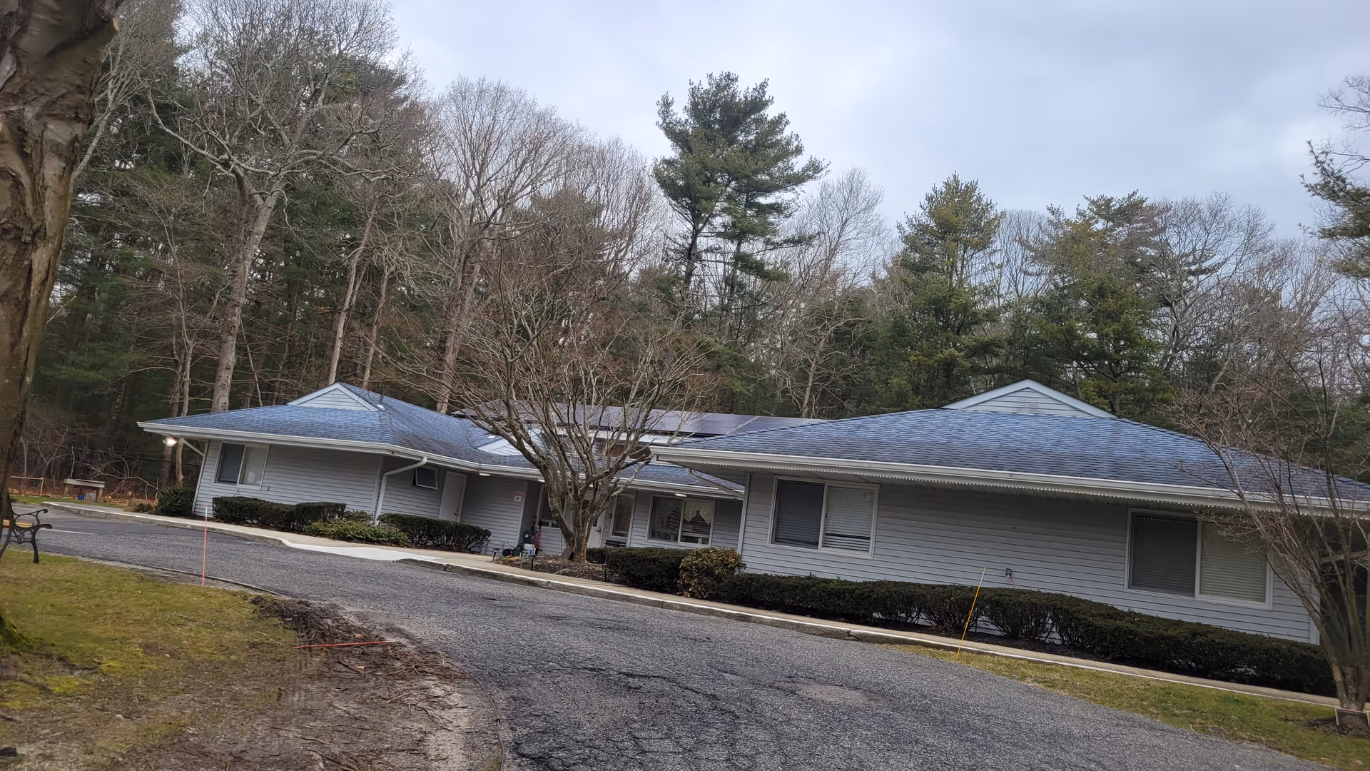 Single-story light gray building with a blue roof, set among trees.