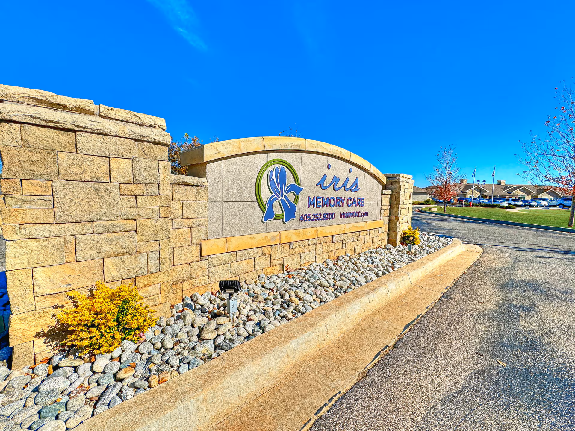 Stone entrance sign for Iris Memory Care with rocks under a blue sky.