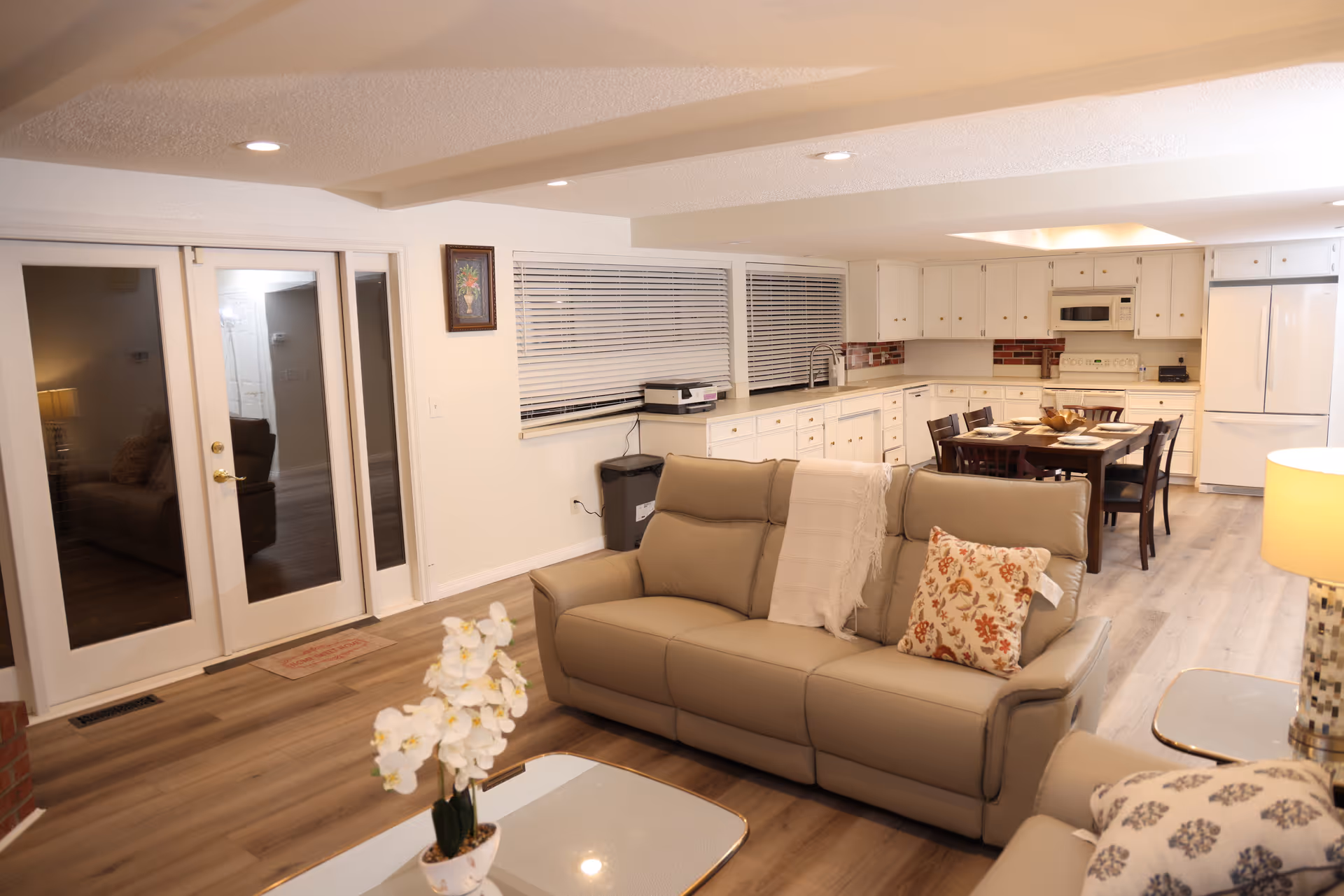Open-concept living area with beige sofa, coffee table, and visible kitchen/dining space.