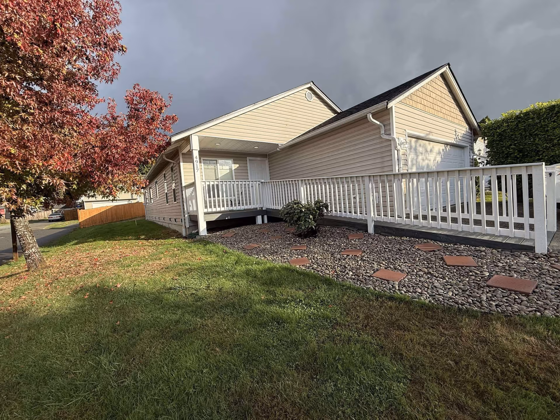 Single-story beige adult family home with ramp, white railing, and landscaped front yard.