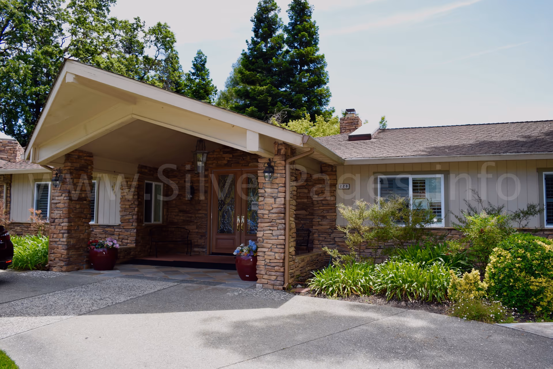 Front entrance of a senior residence with stone pillars, covered porch, and landscaped garden.