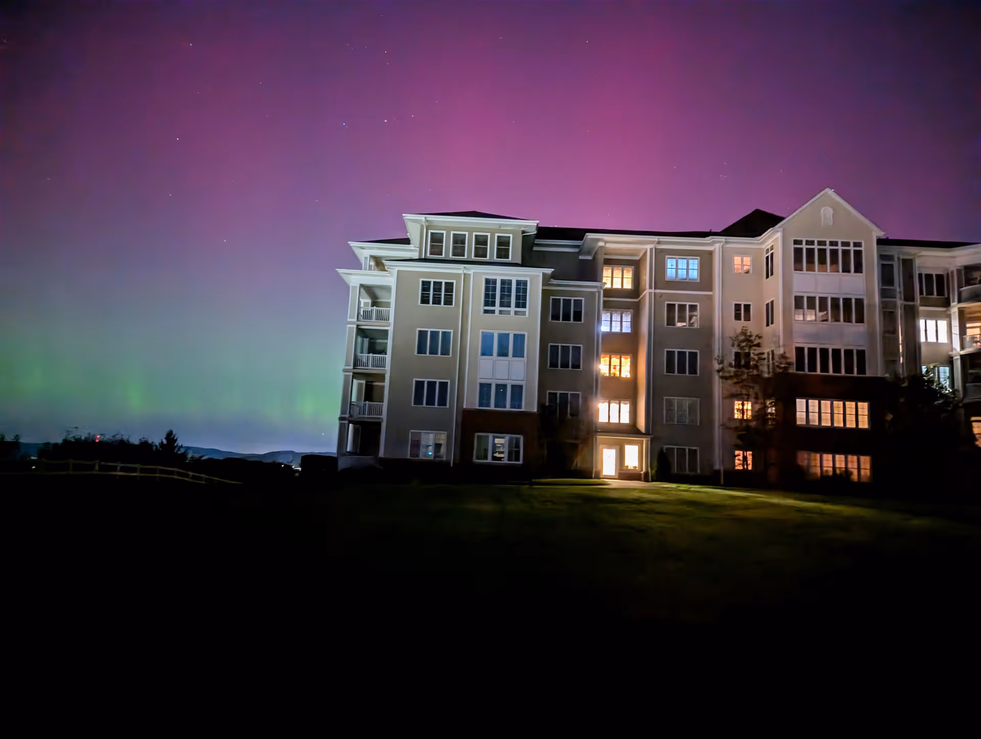 Night view of a multi-story retirement community building with illuminated windows and aurora borealis.