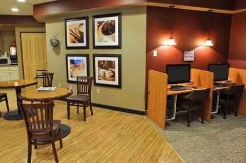 Senior living facility common area with round tables, chairs, and computer workstations.