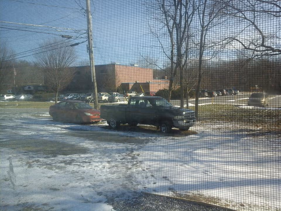 Snow-covered parking lot in front of a brick building viewed through a window screen