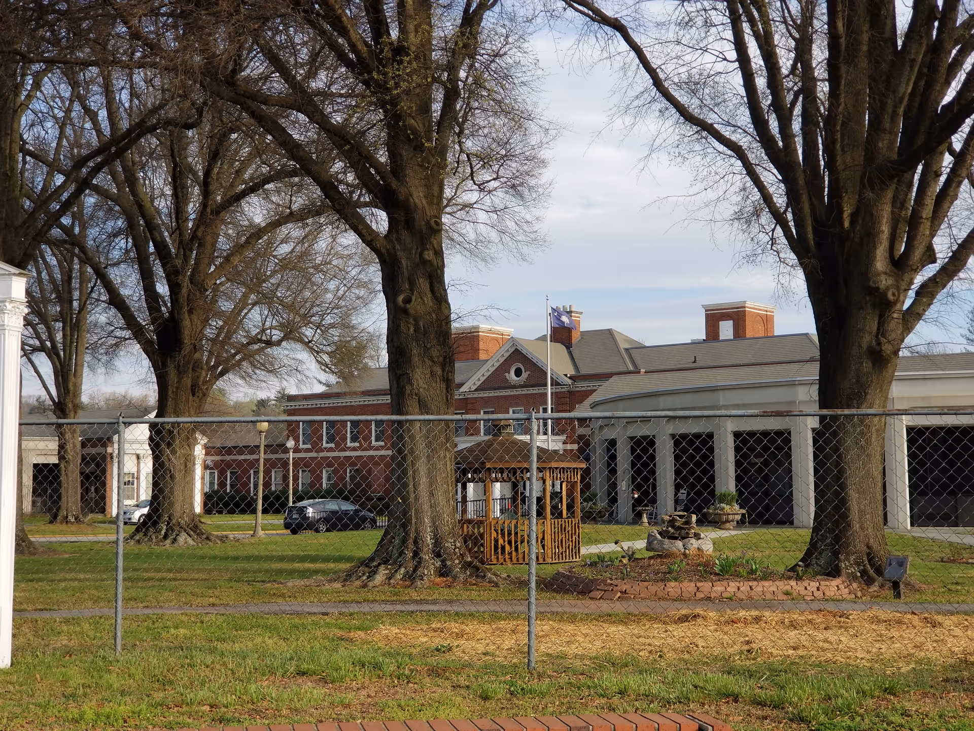 Exterior view of Shepherd's Care Assisted Living Center with trees, fence, and gazebo.