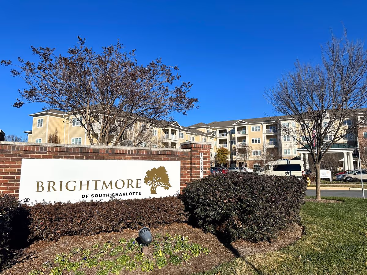 Entrance sign reading 'Brightmore of South Charlotte' in front of a multi-story senior living building under a clear blue sky.