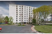 Exterior view of a white multi-story senior living building with trees and circular driveway and parking.