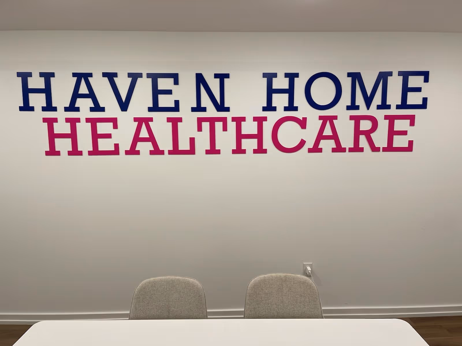 Interior wall with Haven Home Healthcare sign, white table, and two gray chairs.