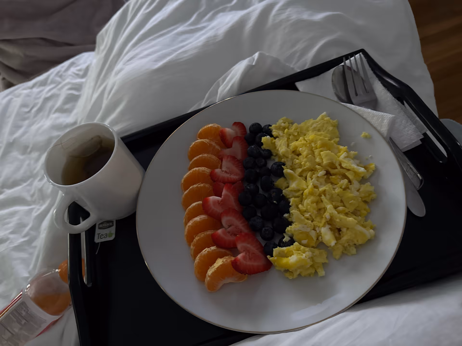 Tray with sliced fruit, scrambled eggs, and tea on a bed in a bright bedroom.