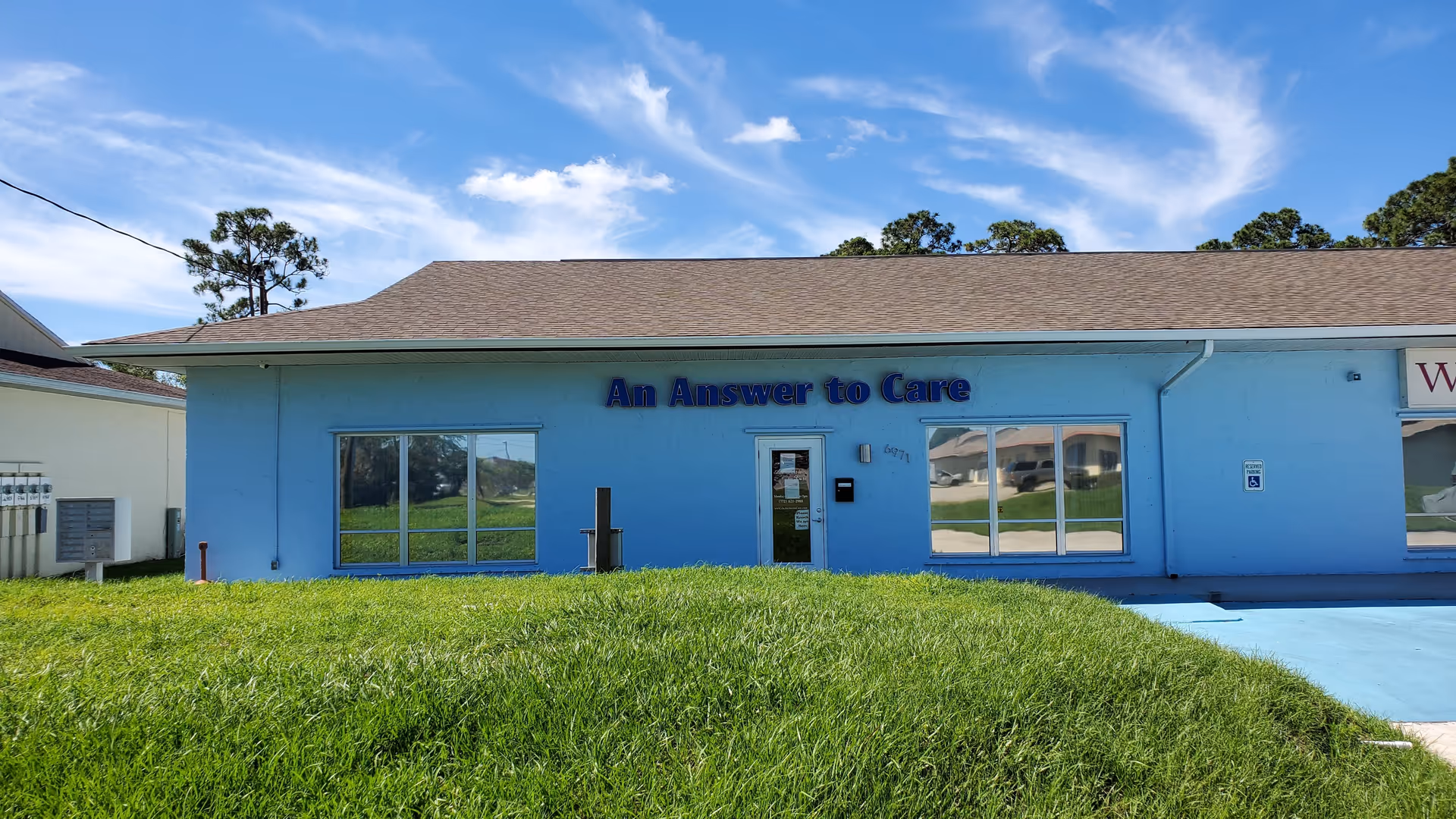 Blue single-story senior facility exterior with sign An Answer to Care and glass windows