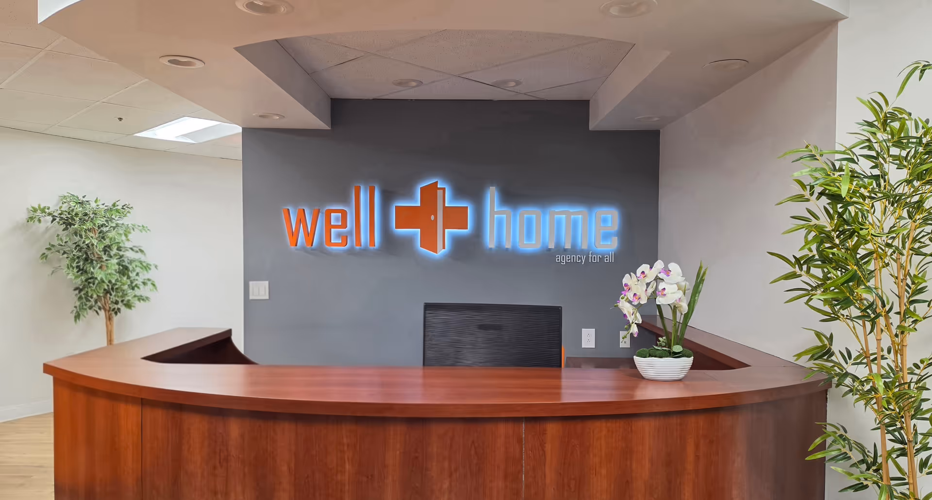 Curved wooden reception desk in a lobby with a neon Well Home sign on the wall.