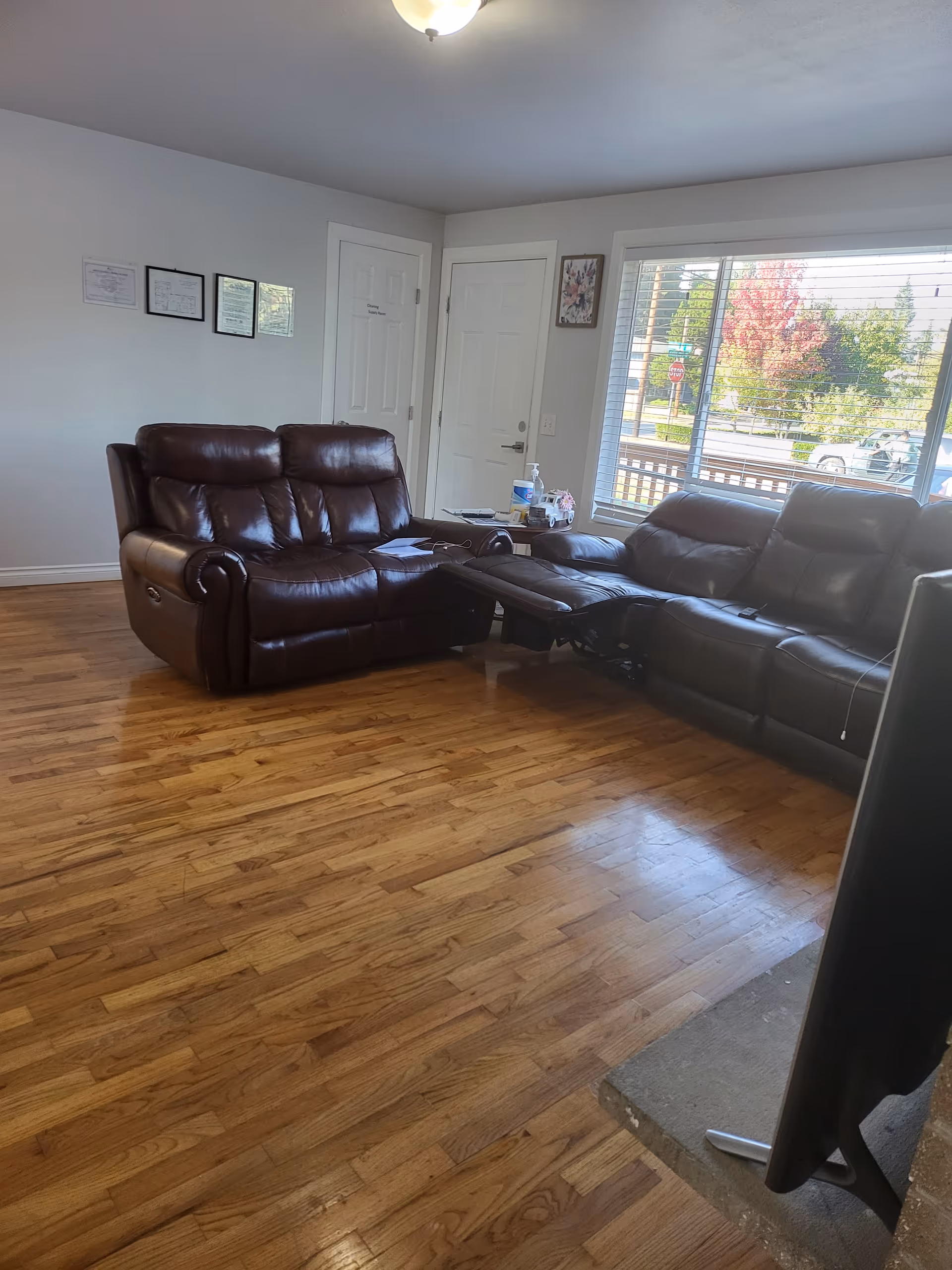 Spacious living room with dark leather sofas, polished hardwood floors, and a large window view.
