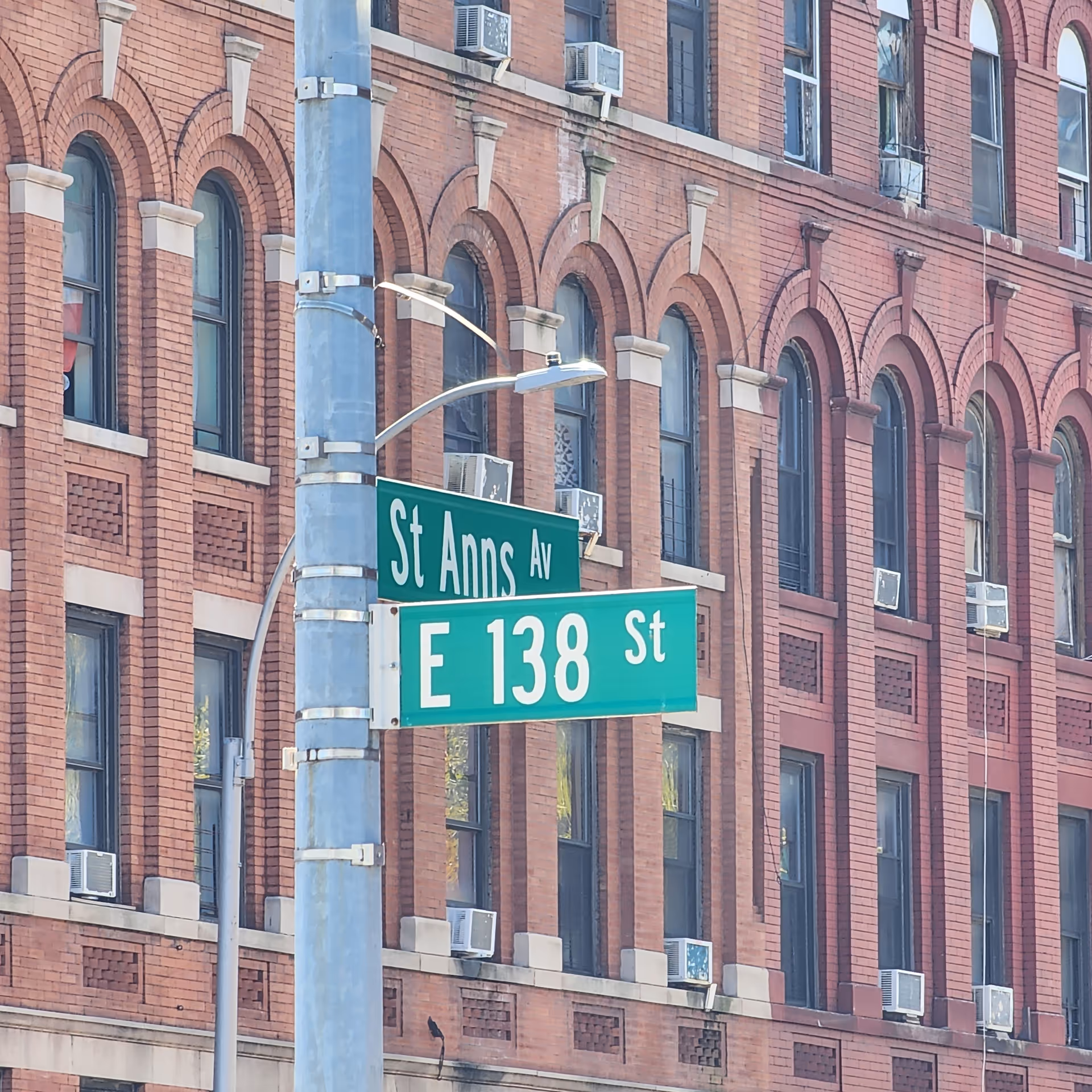 St Ann's Ave and E 138 St street signs on a blue pole before brick building