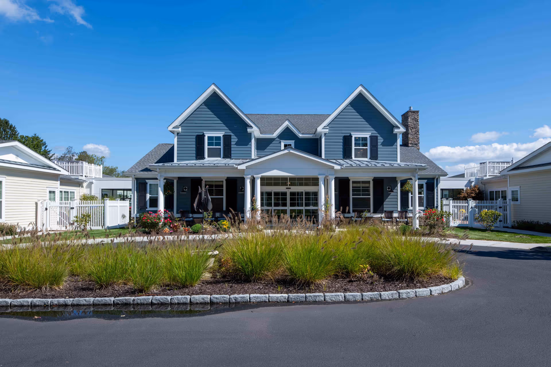 Blue two-story senior living building with a landscaped circular driveway in front.
