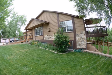Exterior view of a brown and beige senior living facility with a grassy lawn and trees.