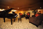 A cozy lounge with a grand piano, red chairs, sofas, and plants.