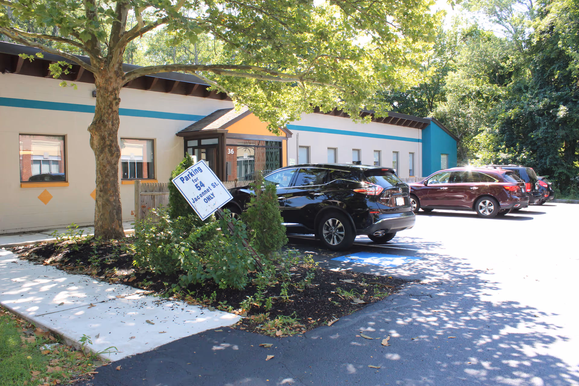 Front exterior of a low-rise facility with a parking lot and trees.