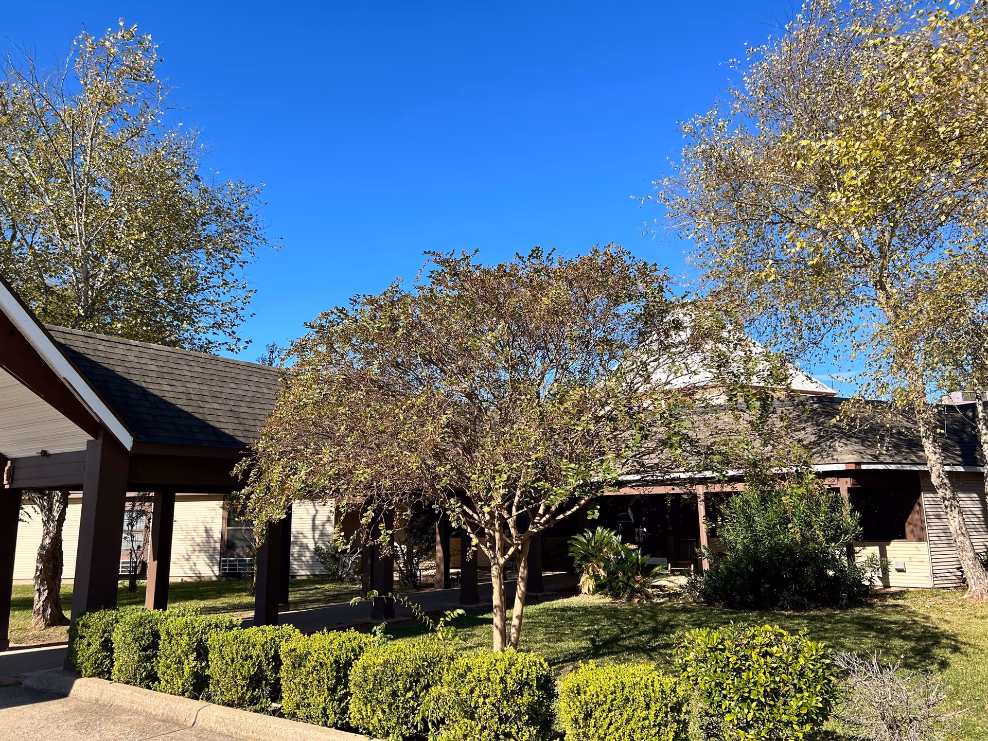 Senior living facility entrance with a covered walkway and manicured bushes under a blue sky