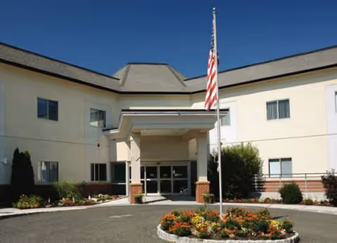 Front entrance of a senior living facility with flag and circular flower bed