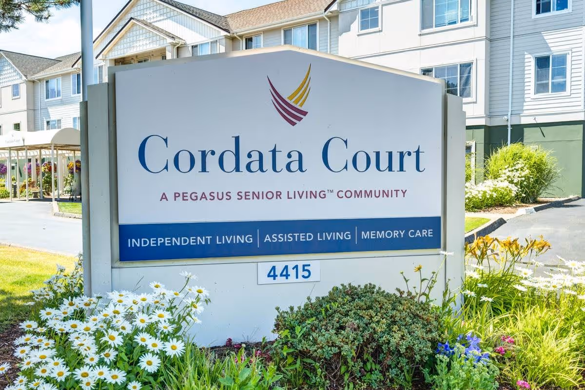 Outdoor view of the Cordata Court senior living community sign with flowers and greenery around it, and the building visible in the background.