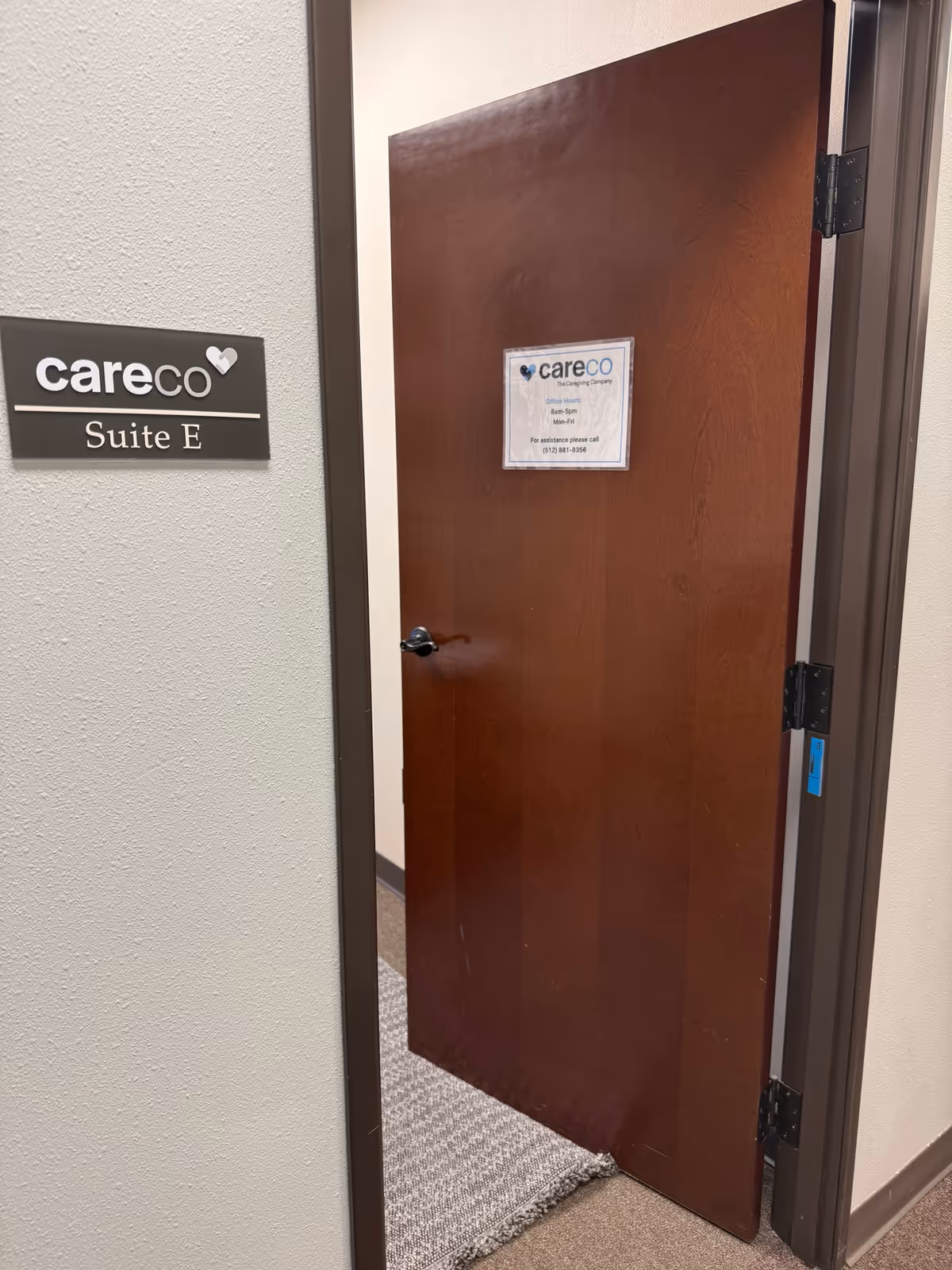 Slightly ajar wooden door labeled Suite E beside a CareCo sign on textured wall.