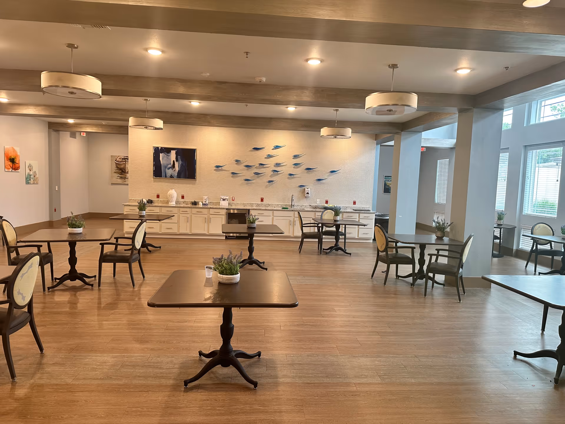 Open, well-lit senior living common area with multiple tables and seating.