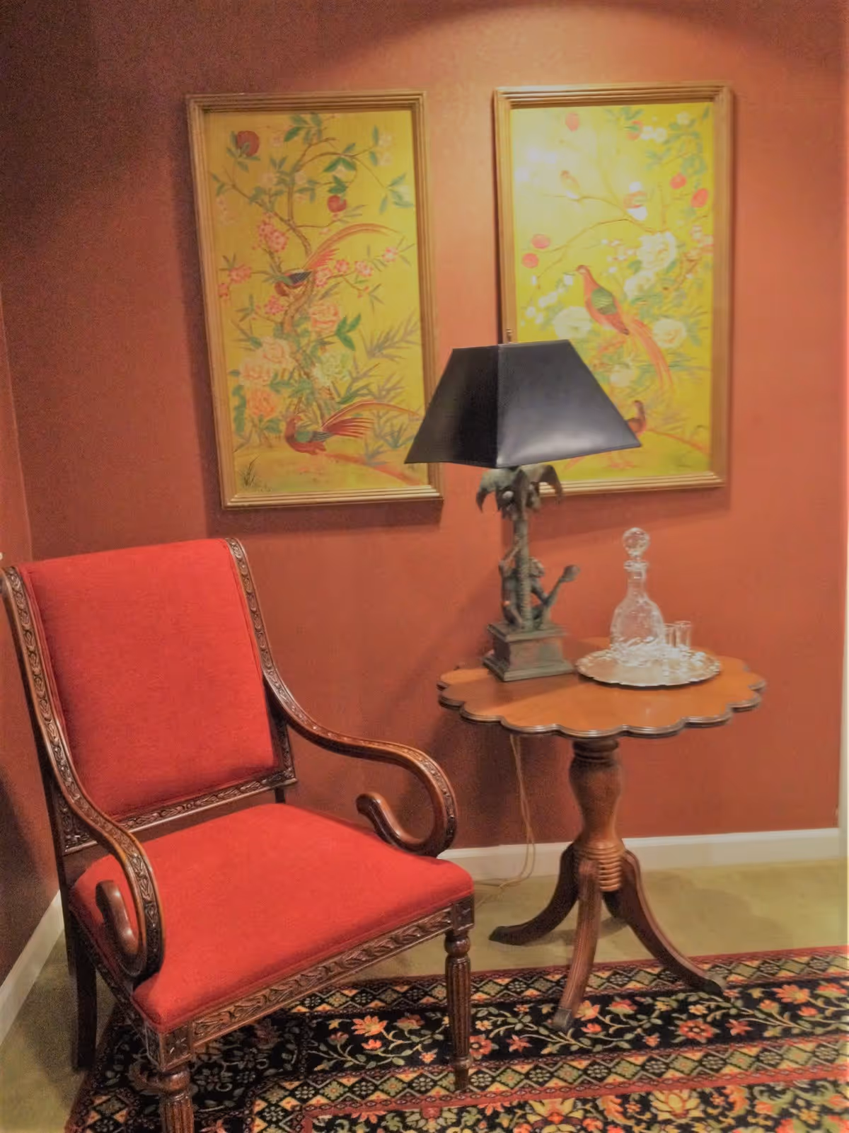 A red upholstered armchair beside a round wooden table with a lamp and decorative rug.